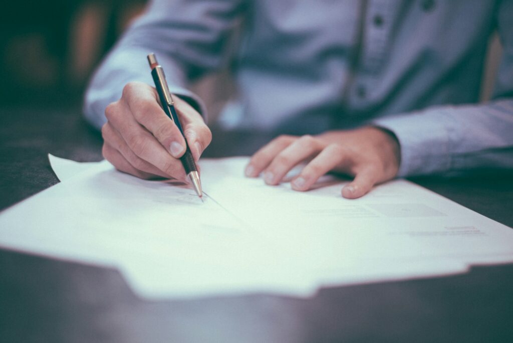 A person writing notes while reviewing paperwork at a desk