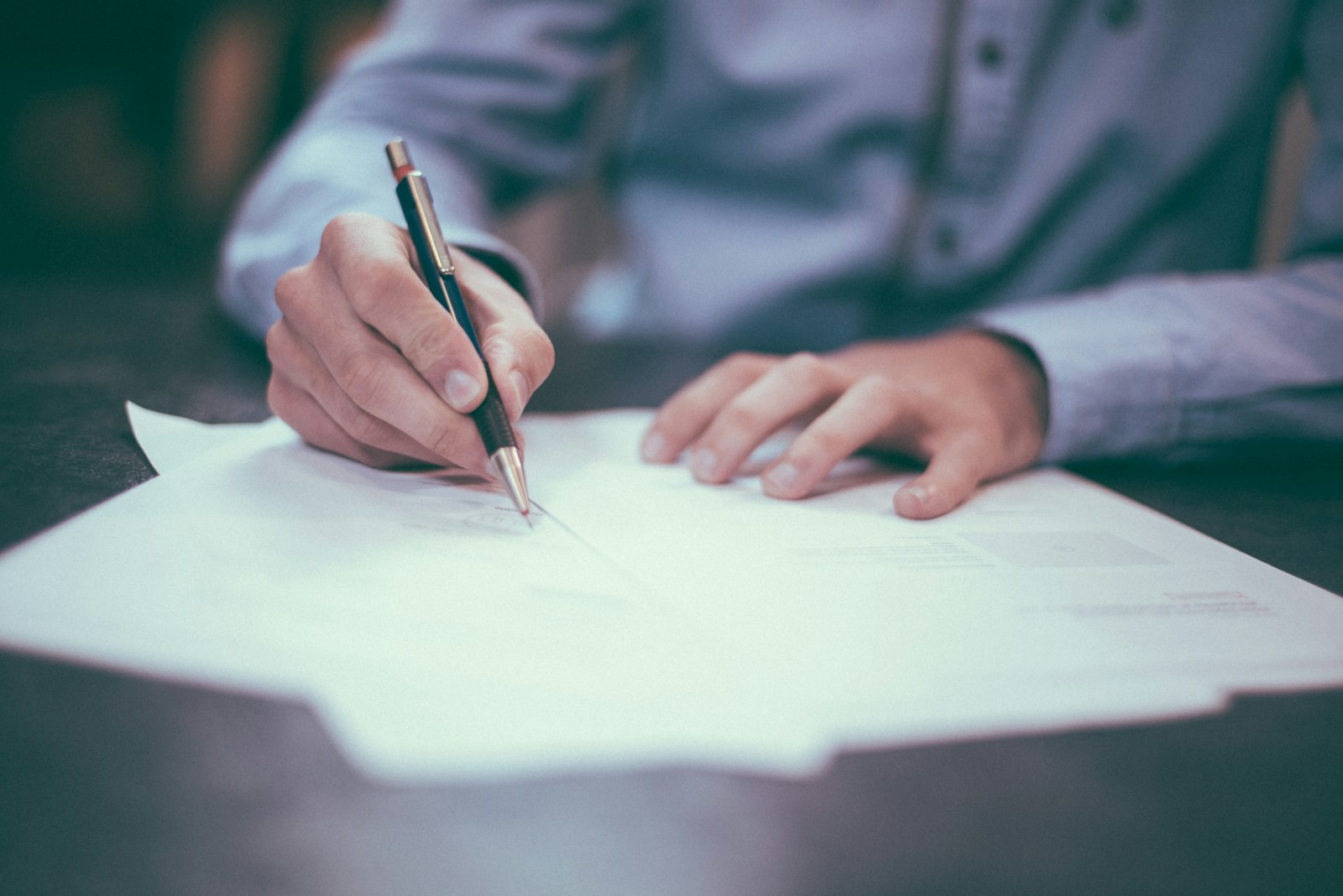 A person writing notes while reviewing paperwork at a desk
