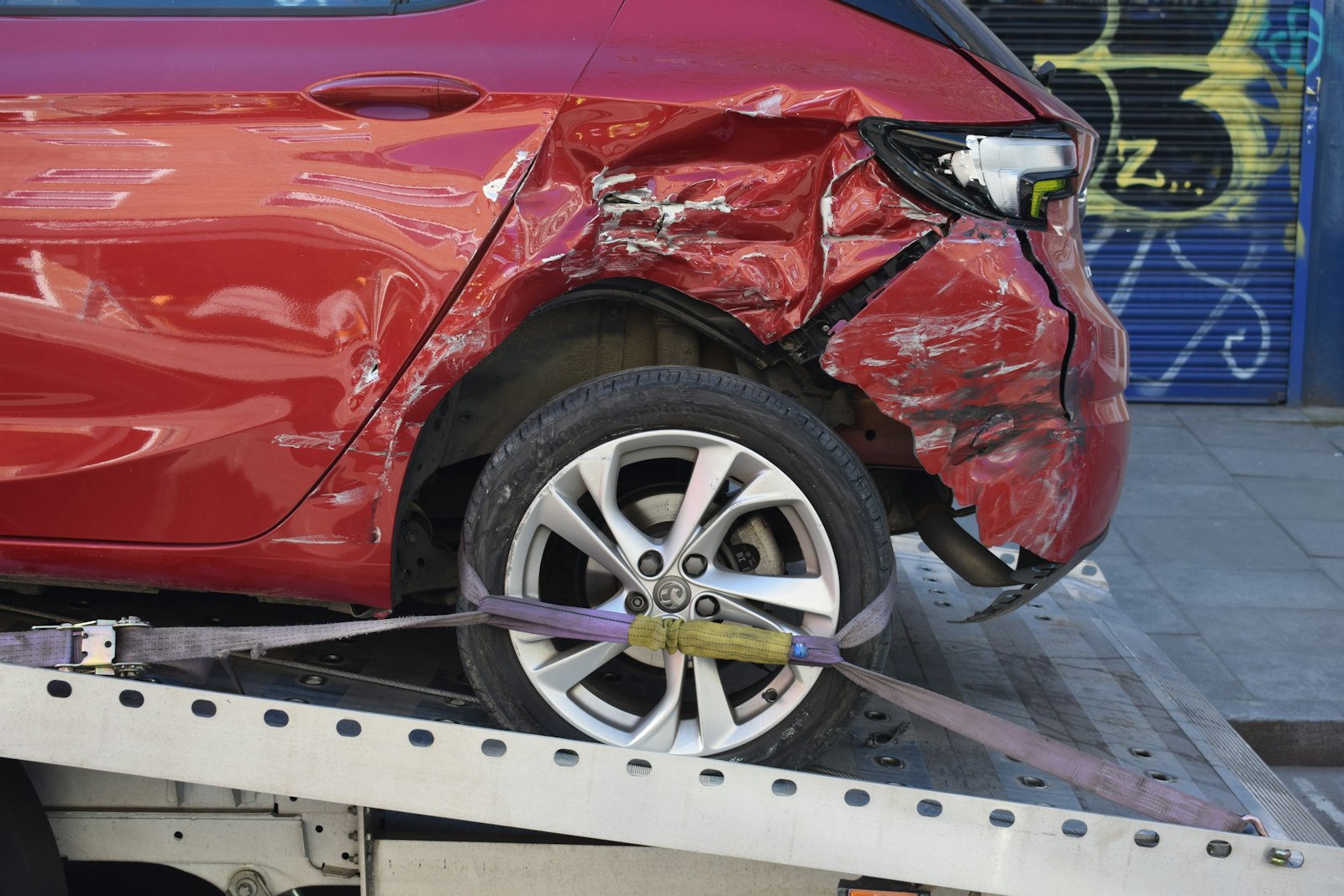A red car being loaded onto a flatbed tow truck after a crash